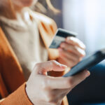 Woman holding a credit card and smartphone while making an online purchase or managing her finances.