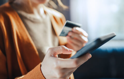 Woman holding a credit card and smartphone while making an online purchase or managing her finances.
