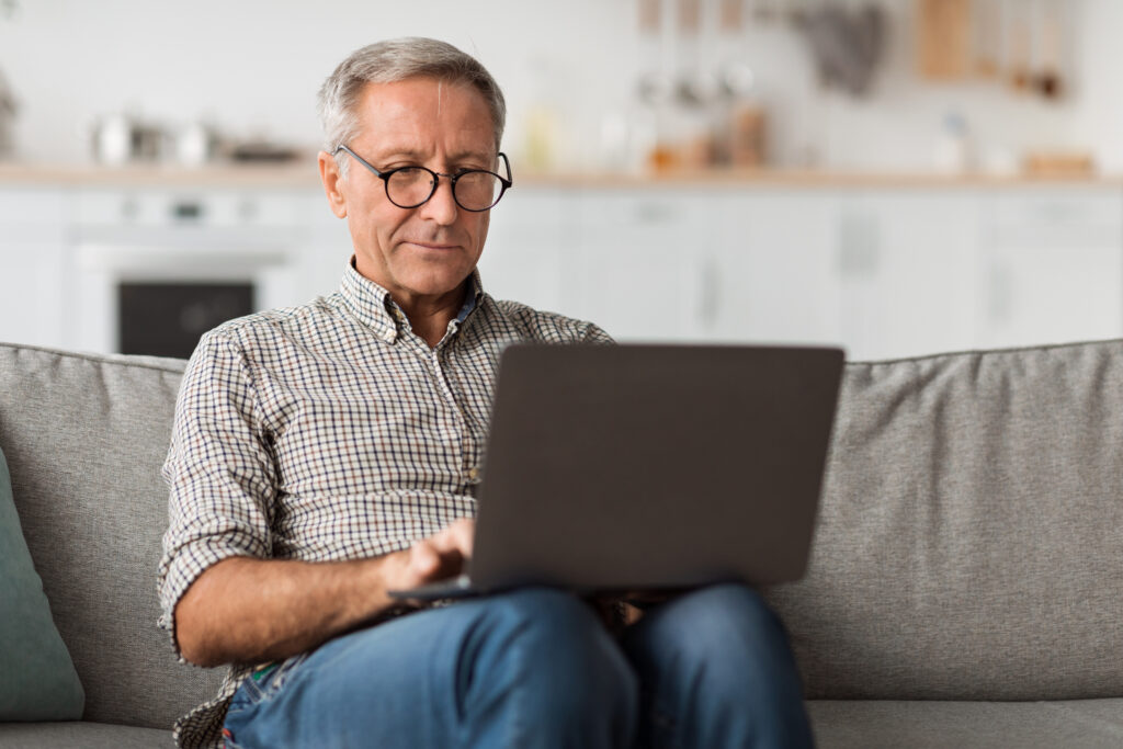 Older man using a laptop while sitting on a couch at home.