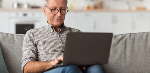 Older man using a laptop while sitting on a couch at home.