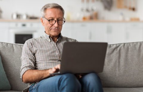 Older man using a laptop while sitting on a couch at home.