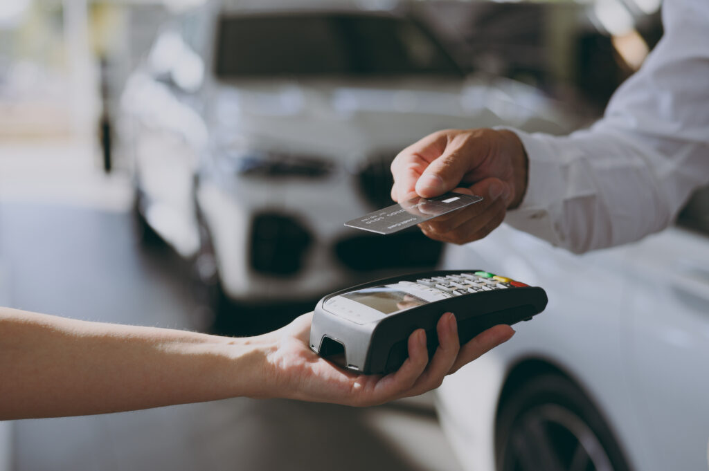 Person using a credit card to make a payment with a card reader at a car dealership, representing vehicle purchases or financing.