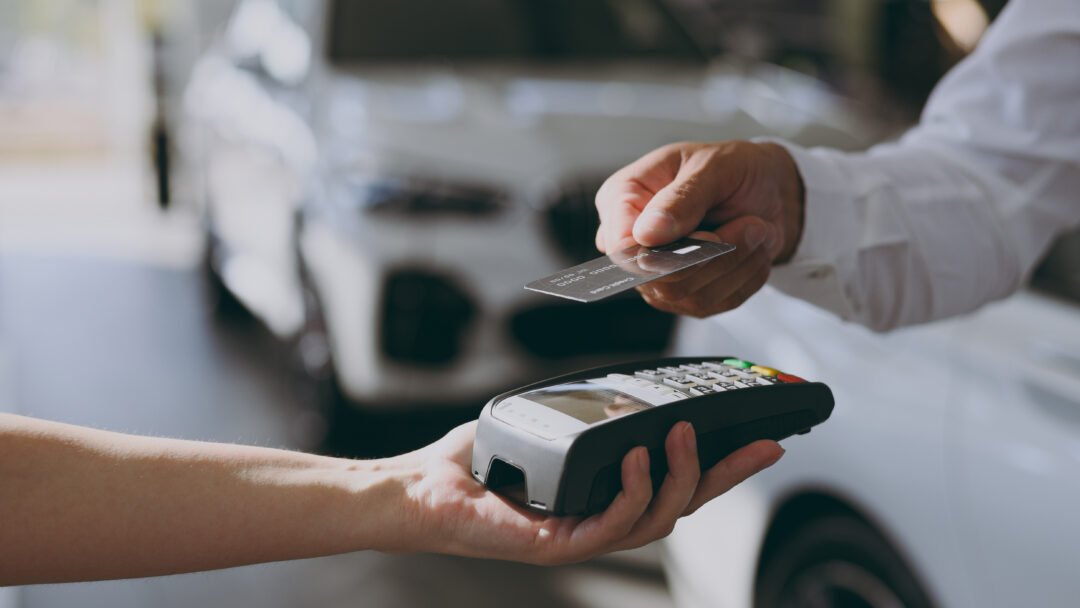Person using a credit card to make a payment with a card reader at a car dealership, representing vehicle purchases or financing.