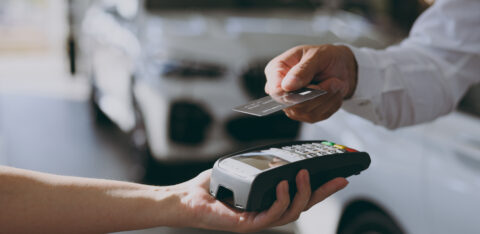 Person using a credit card to make a payment with a card reader at a car dealership, representing vehicle purchases or financing.