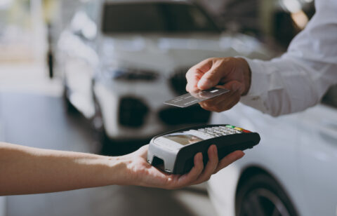 Person using a credit card to make a payment with a card reader at a car dealership, representing vehicle purchases or financing.