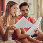 Budget, debt and mortgage with a couple reading bills and documents while checking their expenses and savings. Husband and wife looking worried while reading a loan application or contract together