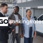 Car dealership scene with a salesperson showing a vehicle to two customers with GOBankingRates image text.