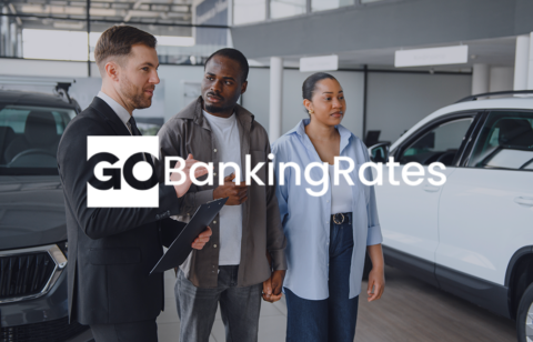 Car dealership scene with a salesperson showing a vehicle to two customers with GOBankingRates image text.