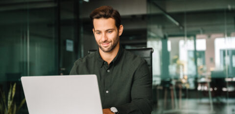 Happy latin hispanic young business man working on laptop computer in company office. Smiling European entrepreneur manager businessman using pc for communication, learning at workplace. Copy space