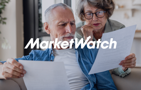 Older couple sitting on a couch reviewing paperwork together with a MarketWatch logo overlay.