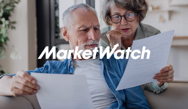 Older couple sitting on a couch reviewing paperwork together with a MarketWatch logo overlay.