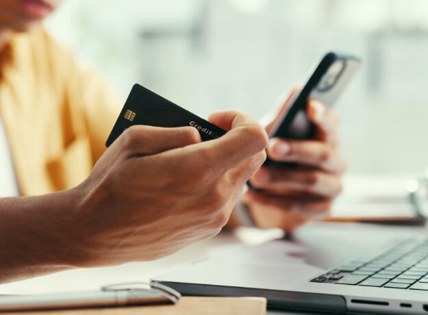 Hands, credit card and laptop at office with phone, online shopping and fintech for easy payment. Person, computer and smartphone with ecommerce, bills or digital bank with customer experience on web