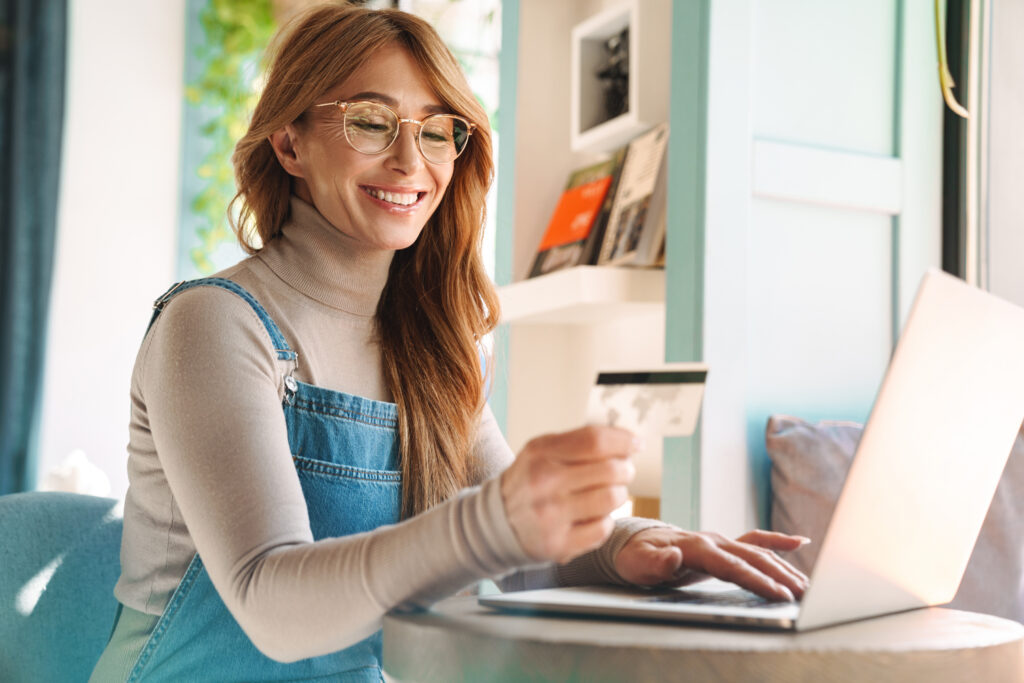 Photo of smiling mature woman holding credit card while using on laptop