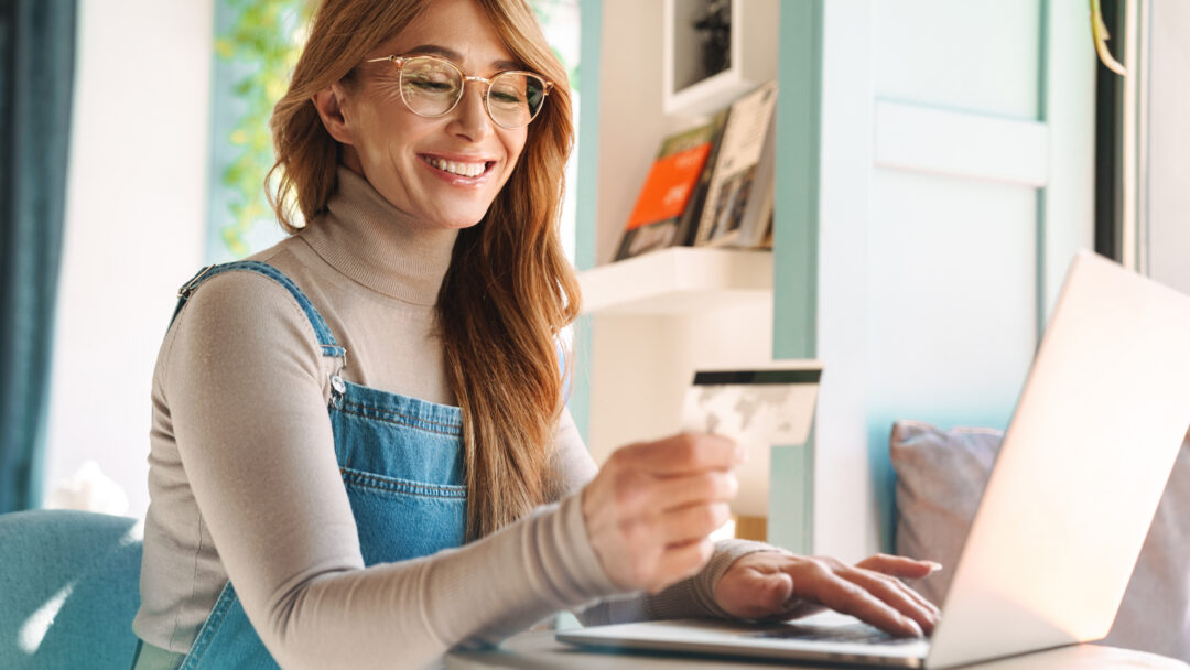 Photo of smiling mature woman holding credit card while using on laptop