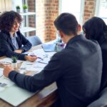 Young beautiful couple applying for mortgage. Sitting smiling happy meeting with real state agent signing mortgage loan at bank