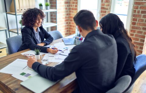 Young beautiful couple applying for mortgage. Sitting smiling happy meeting with real state agent signing mortgage loan at bank