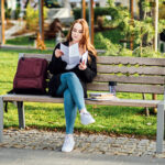 Understanding Student Loan Repayment Options. Pros and Cons of Federal vs Private Student Loans. Young student girl in glasses and with laptop and books reading letter outdoors