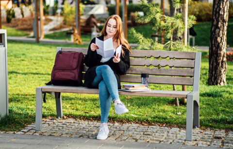 Understanding Student Loan Repayment Options. Pros and Cons of Federal vs Private Student Loans. Young student girl in glasses and with laptop and books reading letter outdoors
