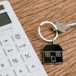Home key with house keyring or keychain with white calculator on wooden table using as mortgage calculation or buy and sell property and real estate