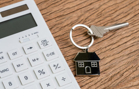 Home key with house keyring or keychain with white calculator on wooden table using as mortgage calculation or buy and sell property and real estate