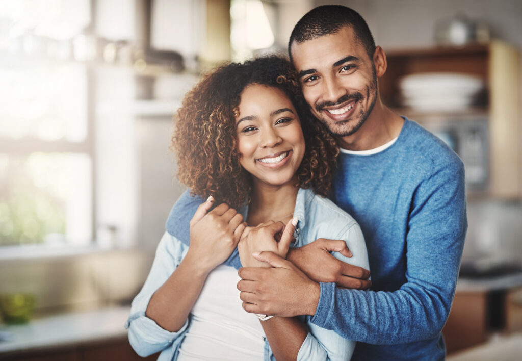 Love, portrait and happy couple hug in kitchen of home with smile, embrace and healthy relationship. Happiness, man and woman hugging in affection, romance and care in marriage, young people in house