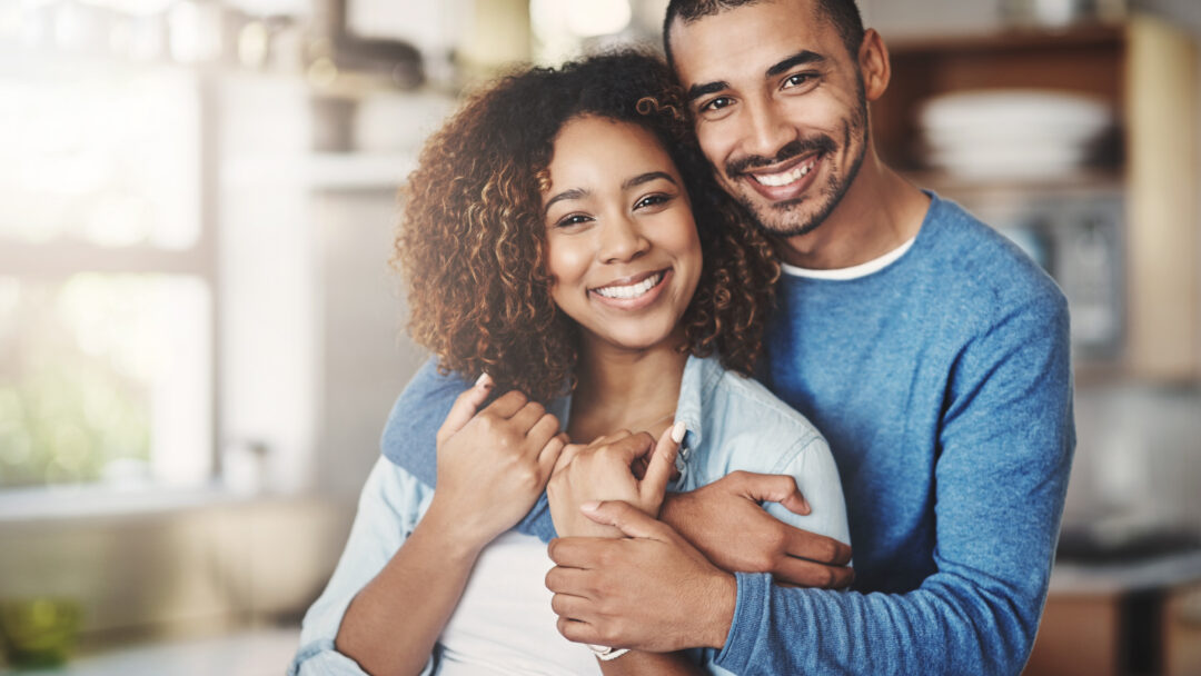 Love, portrait and happy couple hug in kitchen of home with smile, embrace and healthy relationship. Happiness, man and woman hugging in affection, romance and care in marriage, young people in house