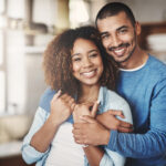 Love, portrait and happy couple hug in kitchen of home with smile, embrace and healthy relationship. Happiness, man and woman hugging in affection, romance and care in marriage, young people in house