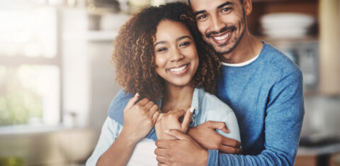 Love, portrait and happy couple hug in kitchen of home with smile, embrace and healthy relationship. Happiness, man and woman hugging in affection, romance and care in marriage, young people in house