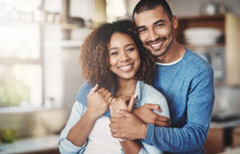 Love, portrait and happy couple hug in kitchen of home with smile, embrace and healthy relationship. Happiness, man and woman hugging in affection, romance and care in marriage, young people in house