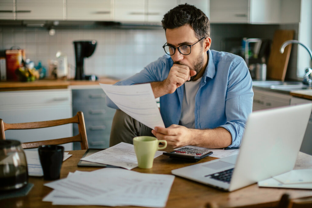 Worried young Caucasian man going over his bills and home finances in the morning in the kitchen