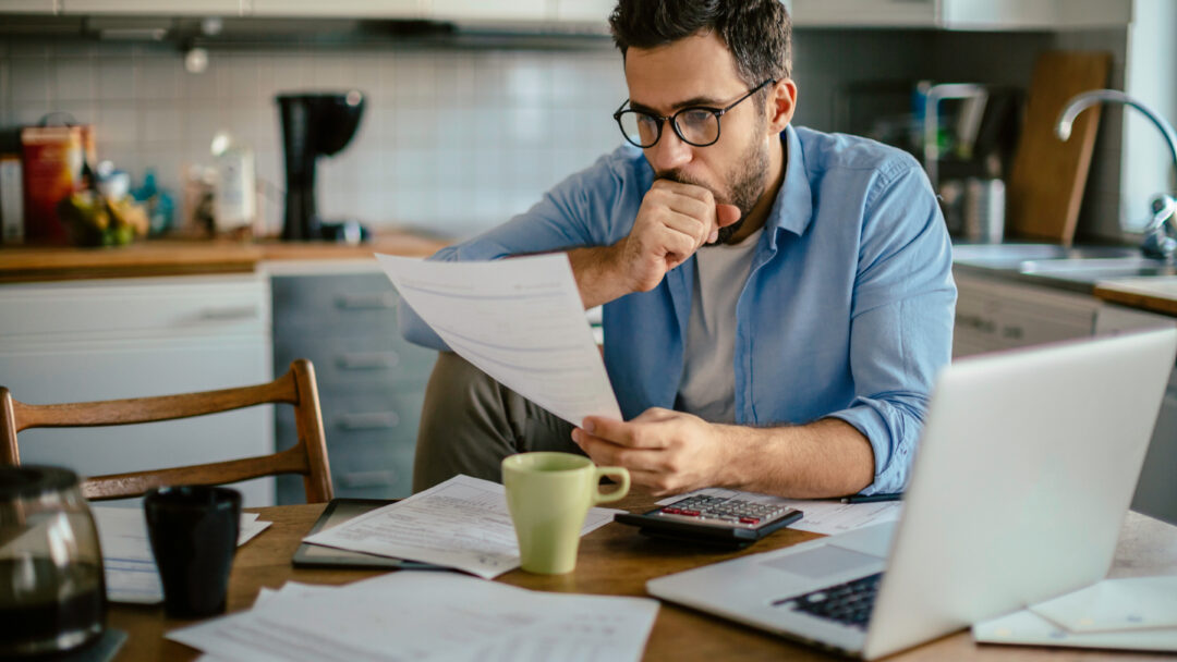 Worried young Caucasian man going over his bills and home finances in the morning in the kitchen