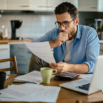 Worried young Caucasian man going over his bills and home finances in the morning in the kitchen