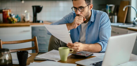 Worried young Caucasian man going over his bills and home finances in the morning in the kitchen