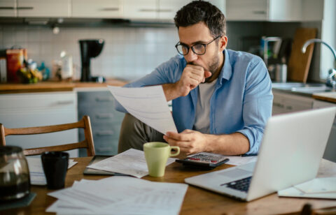 Worried young Caucasian man going over his bills and home finances in the morning in the kitchen