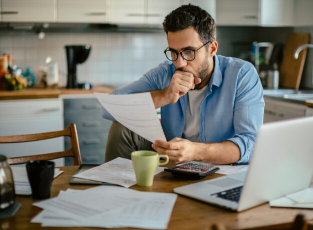 Worried young Caucasian man going over his bills and home finances in the morning in the kitchen