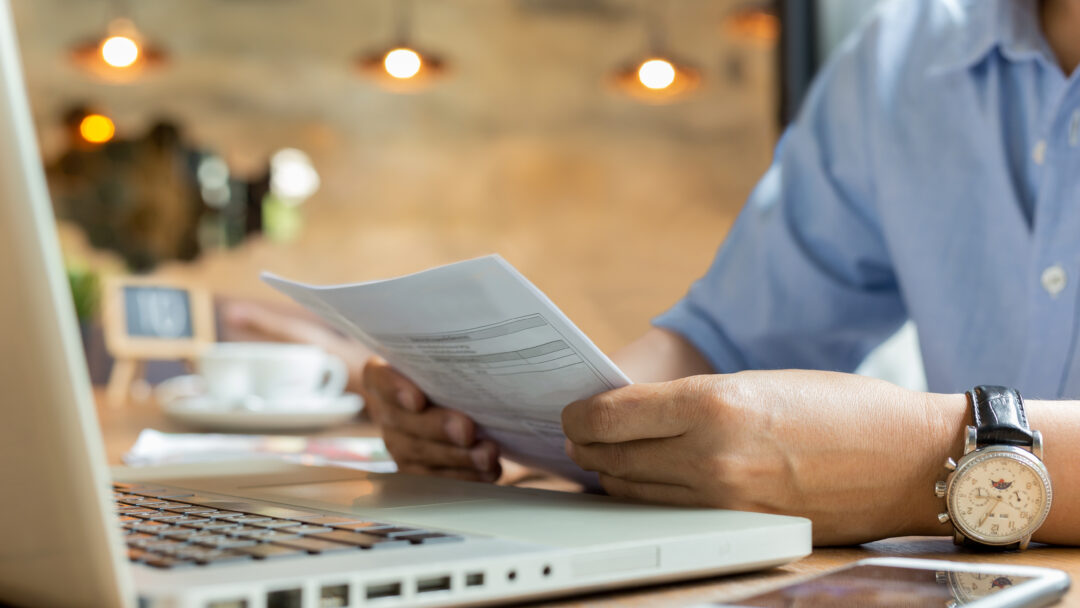 Businessman using laptop while looking at invoice.