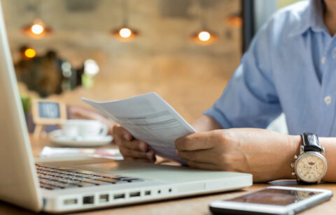 Businessman using laptop while looking at invoice.