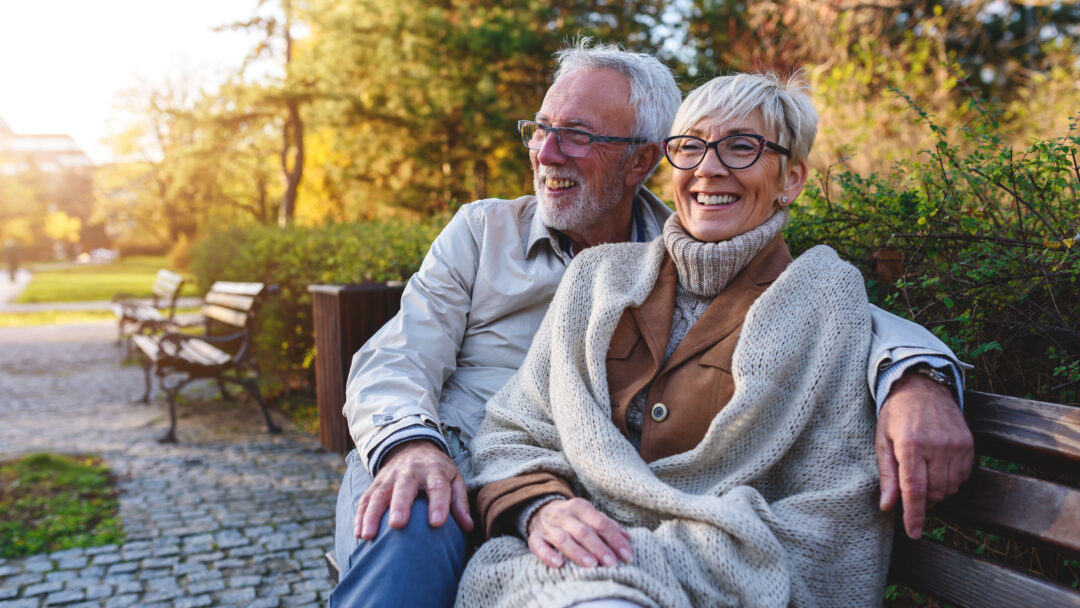 Smiling senior couple sitting on the bench in the park together