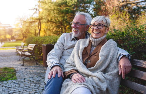 Smiling senior couple sitting on the bench in the park together