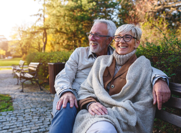Smiling senior couple sitting on the bench in the park together