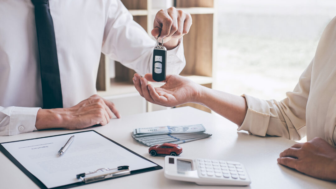 Agent holding key of new car giving to woman client after signing contract