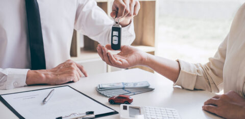 Agent holding key of new car giving to woman client after signing contract