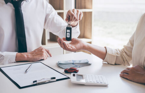 Agent holding key of new car giving to woman client after signing contract