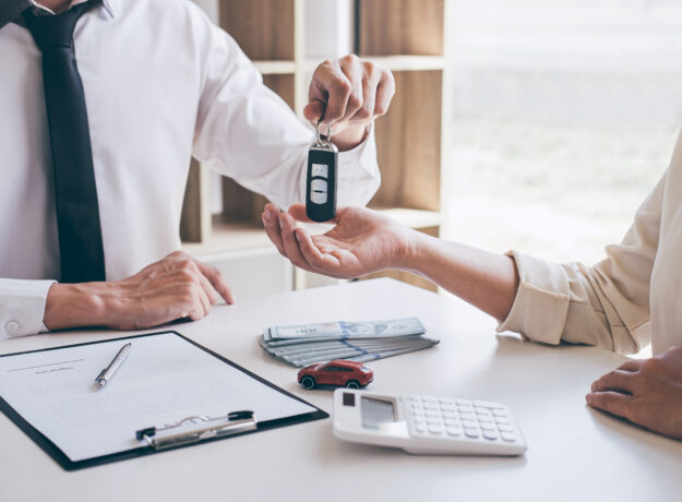 Agent holding key of new car giving to woman client after signing contract