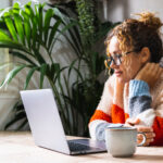 Serene young mature woman looking and reading on laptop online n