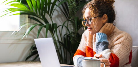 Serene young mature woman looking and reading on laptop online n