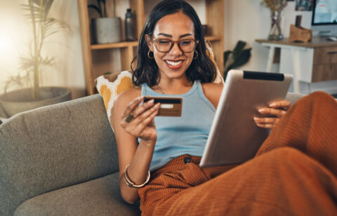 Ecommerce, credit card and woman on a couch, tablet or payment with an order, home or online shopping. Female person, girl or customer on a sofa, technology or buying products with retail or banking