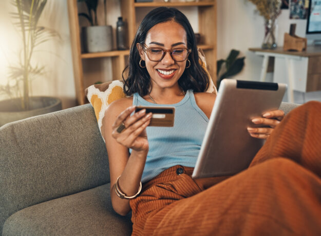 Ecommerce, credit card and woman on a couch, tablet or payment with an order, home or online shopping. Female person, girl or customer on a sofa, technology or buying products with retail or banking