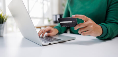 A person is engaged in online shopping, holding a credit card in one hand and typing on a laptop with the other, showcasing modern digital transaction habits.