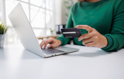 A person is engaged in online shopping, holding a credit card in one hand and typing on a laptop with the other, showcasing modern digital transaction habits.